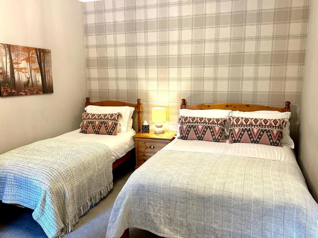 a bedroom with two beds and a table with a lamp at Beechtree Cottage, Ardle Family Room, Kirkmichael in Kirkmichael