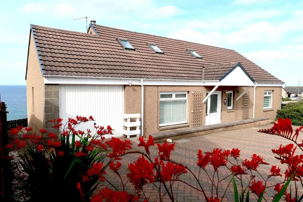 a house with red flowers in front of it at Bright comfy home, sea views and big skies in Banff