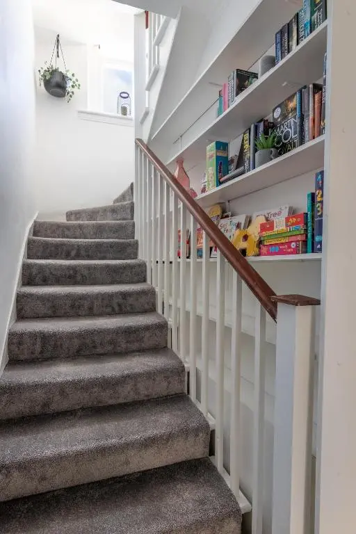 a staircase with grey carpeting and bookshelves at Ness Heights, Spacious City Centre Townhouse in Inverness