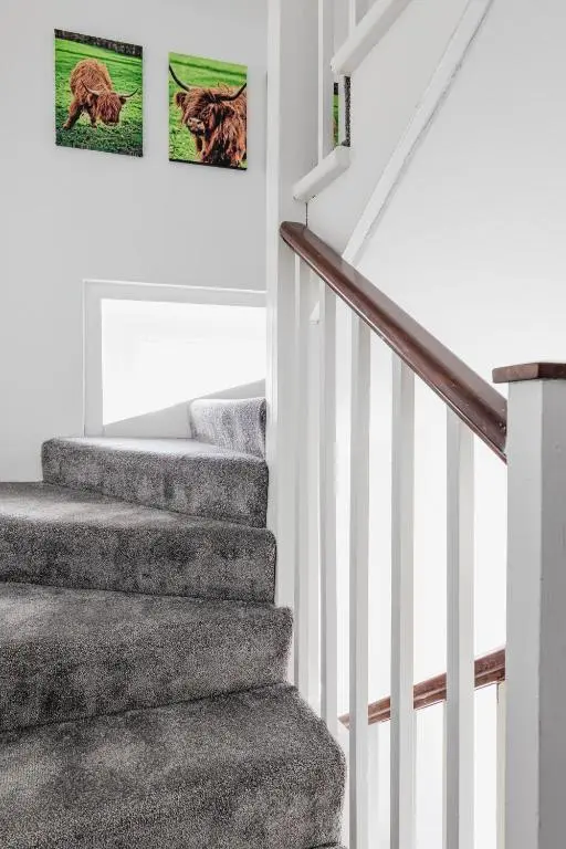 a staircase with grey carpeting and two pictures on the wall at Ness Heights, Spacious City Centre Townhouse in Inverness