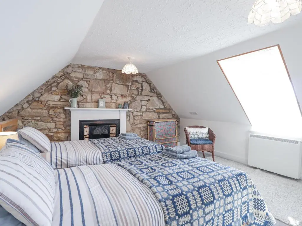 a bedroom with a large bed and a stone wall at Fuchsia Cottage in Fortrose