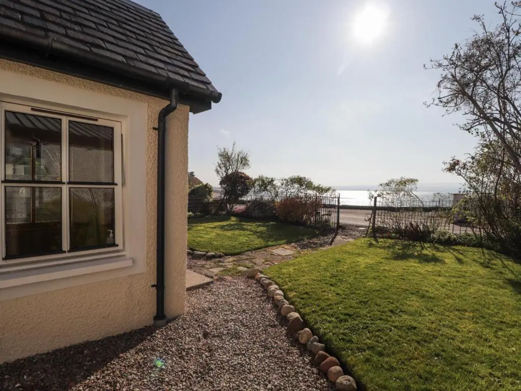 a house with a window and a grass yard at Fuchsia Cottage in Fortrose