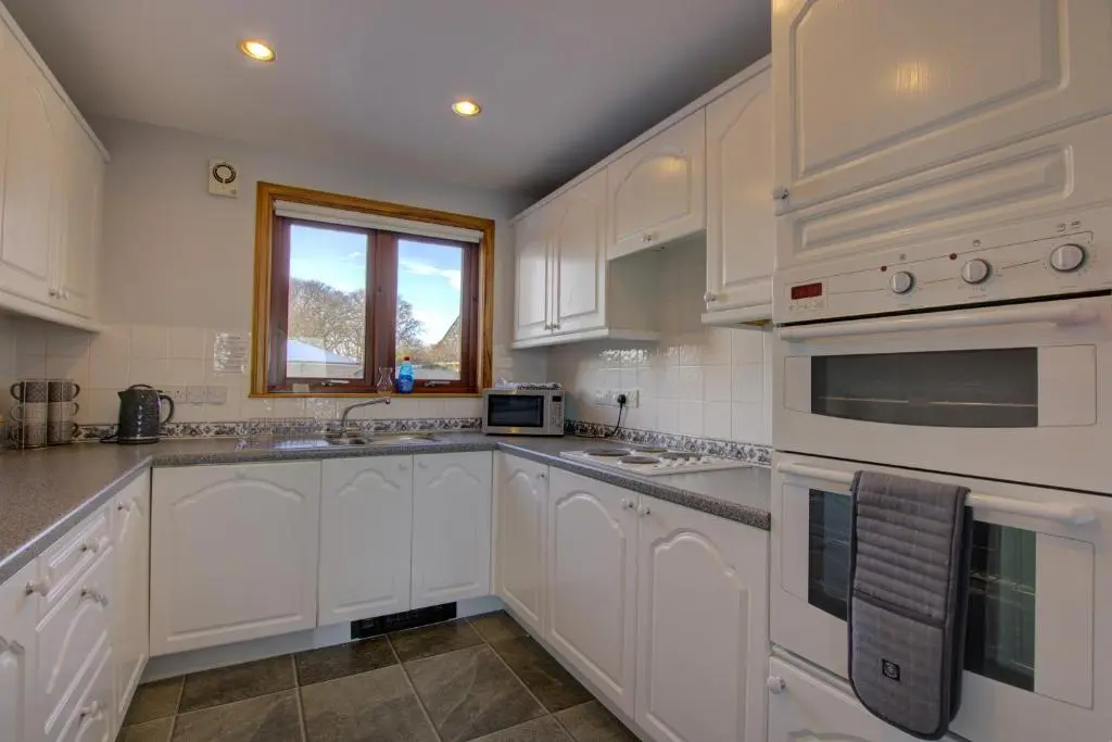 a white kitchen with white cabinets and a window at 2 Links View, Brora in Brora