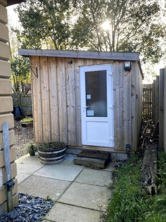 a wooden shed with a white door in a yard at An Cabar - Cabin in Aviemore, Cairngorms NP in Aviemore