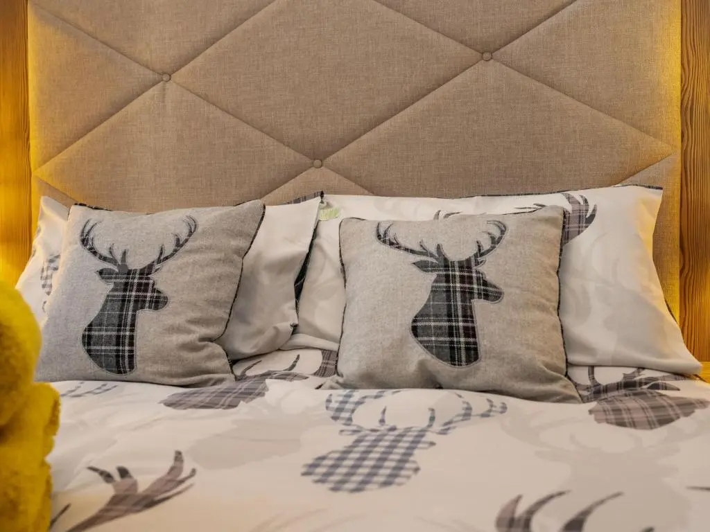 a bed with four pillows and a headboard with at Chalet Monarch by Interhome in Aviemore