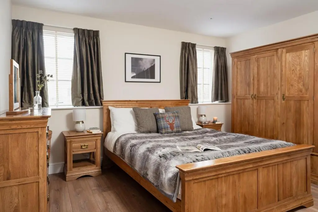 a bedroom with a large bed with wooden furniture and windows at The Old Smithy - Seasgair Lodges in Nethy Bridge