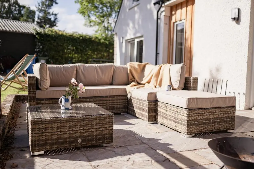 a wicker couch and a table on a patio at The Old Smithy - Seasgair Lodges in Nethy Bridge