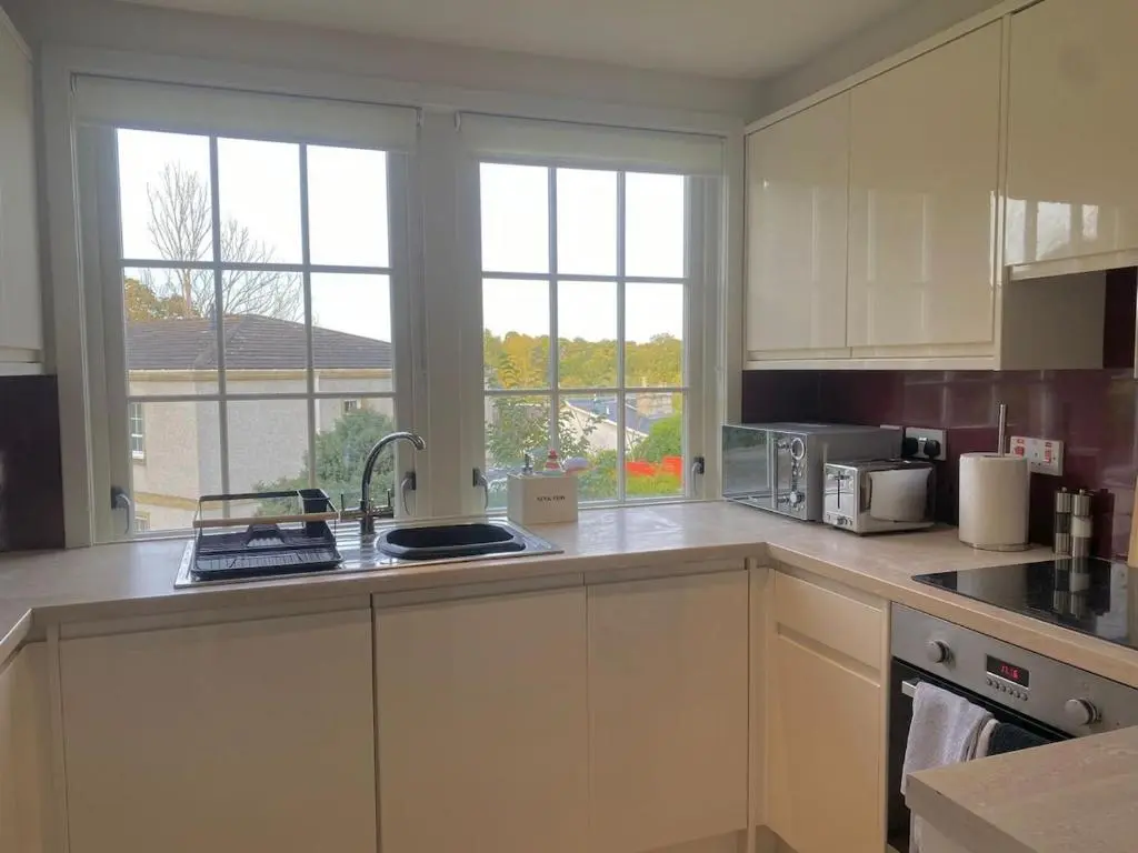 a kitchen with white cabinets and a sink and windows at Warm, stylish 2-bed in Crown, Inverness in Inverness