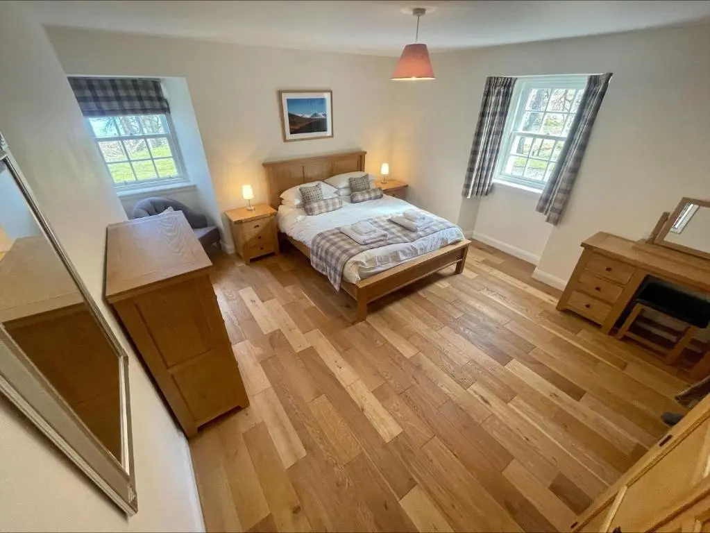 a bedroom with a bed and two windows at Sherrabeg Cottage in Laggan