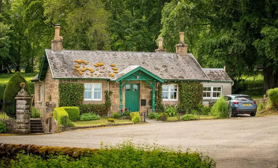 a small house with a green door in a driveway at Foulis Castle Gate Lodge in Evanton