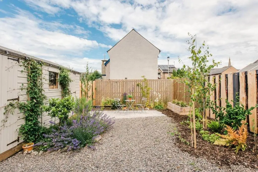 a garden with a white house and a fence at Weavers Cottage in Inverness