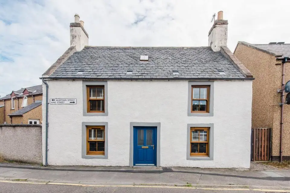 a white house with a blue door on a street at Weavers Cottage in Inverness