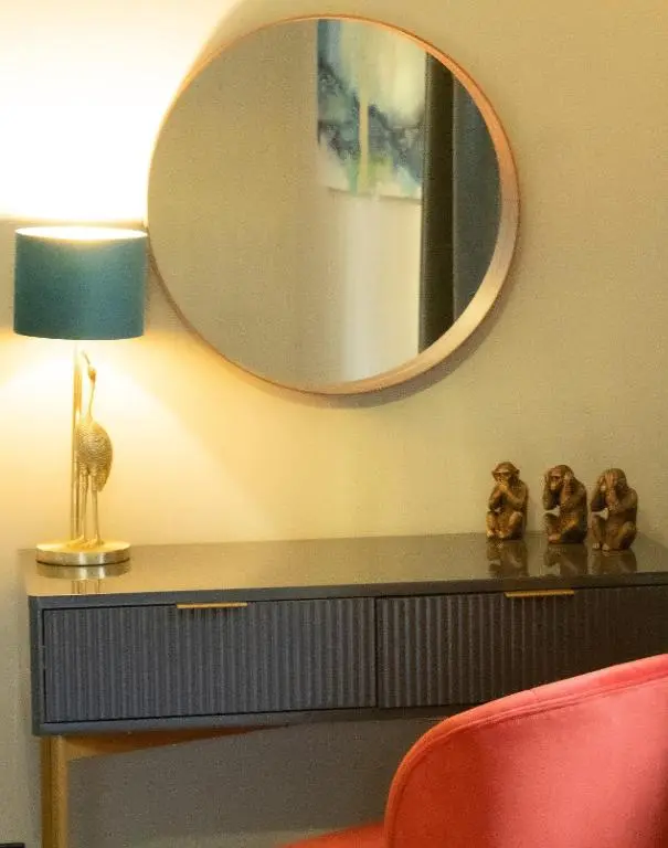 a mirror above a table with a lamp and a chair at Telford Cottage in Kincraig