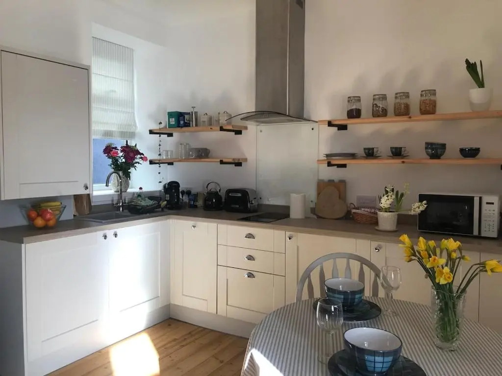 a kitchen with white cabinets and a table with flowers at River Retreat - Riverside Apartment in Inverness City Centre in Inverness