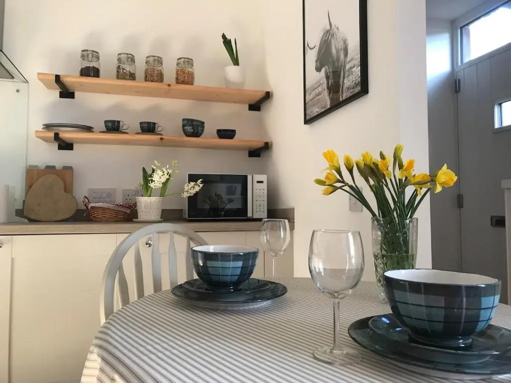 a dining room table with two glasses and a vase of flowers at River Retreat - Riverside Apartment in Inverness City Centre in Inverness