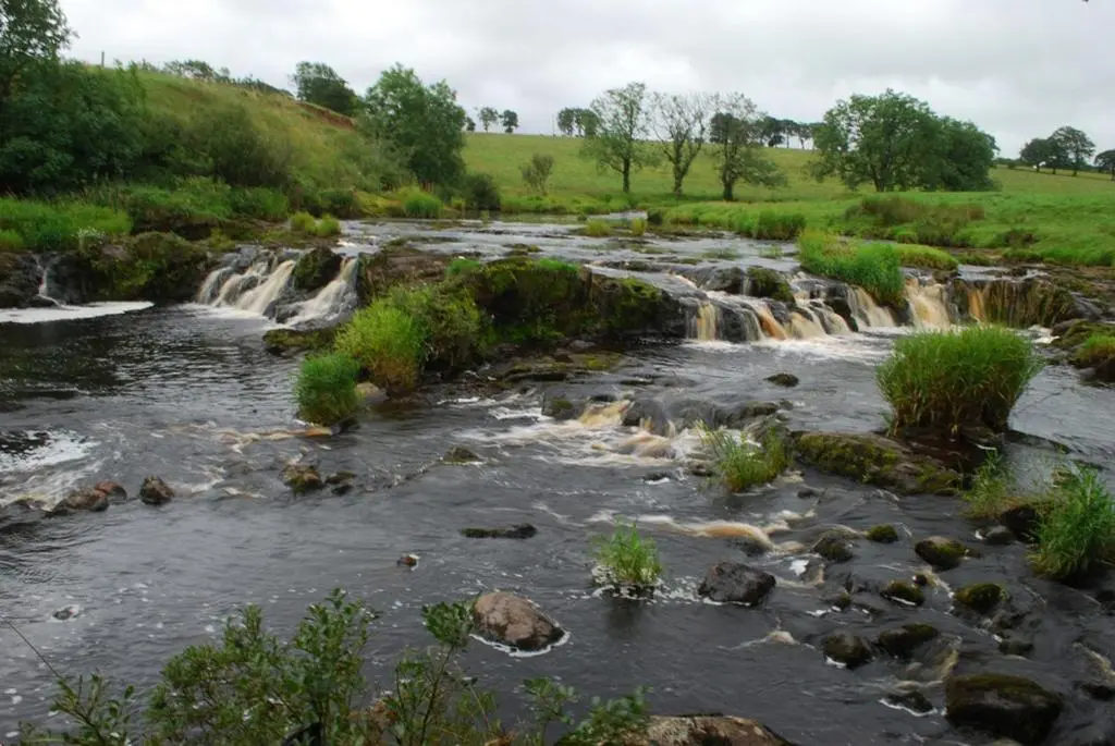 a river with rocks and waterfalls at Swiss Cottage in Ballindalloch