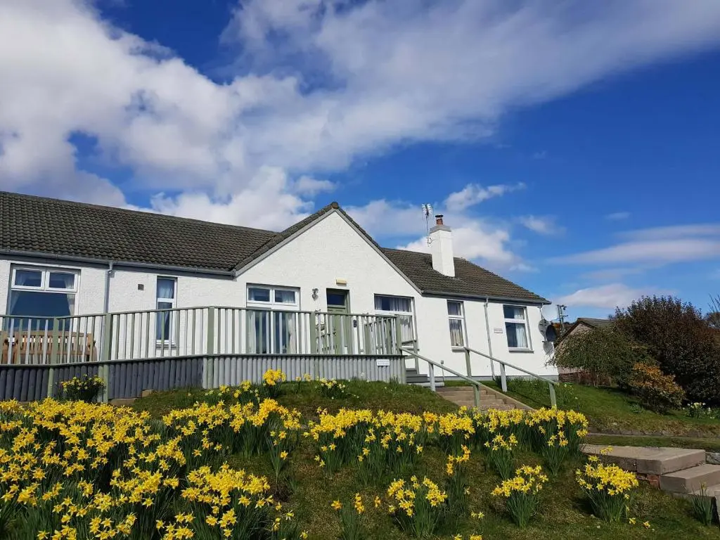 a white house with yellow flowers in front of it at Strathview Lodge B&B in Dornoch