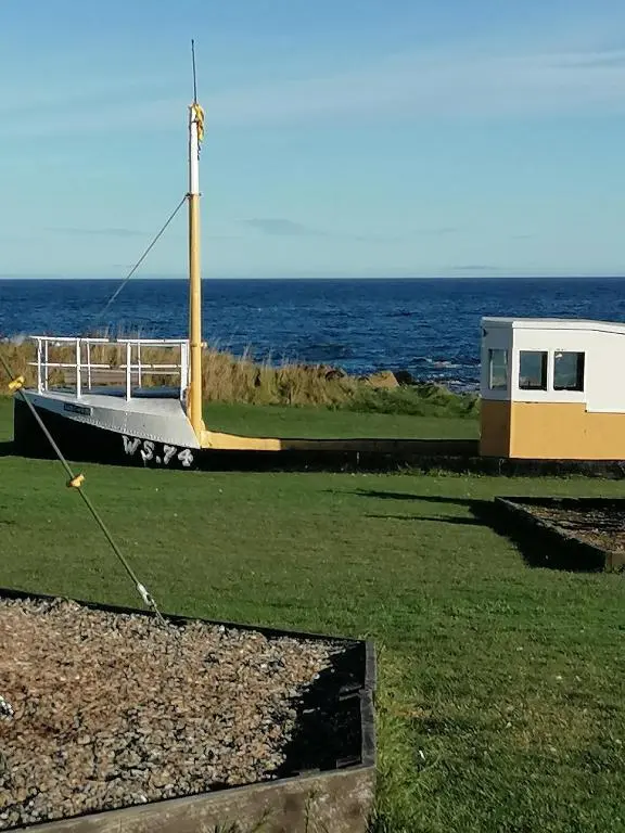a small boat on the grass near the ocean at Hytheview Cottage Whitehills in Whitehills