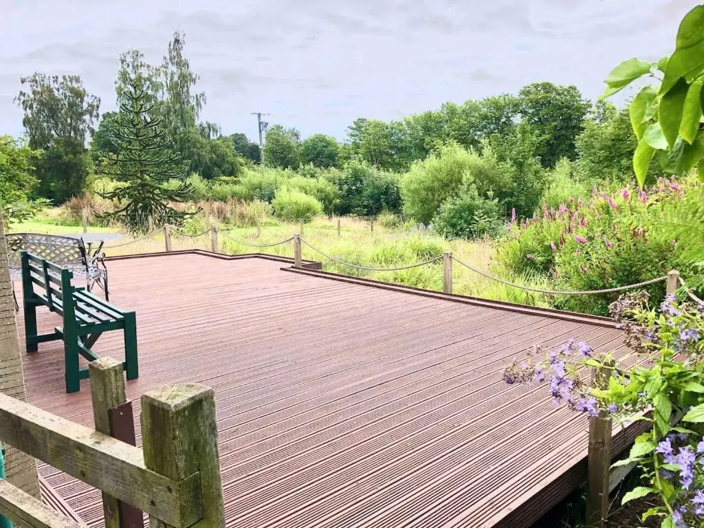 a wooden boardwalk with a bench on top of a field at Canal Side Cottage,on the banks of the Caledonian Canal in Inverness