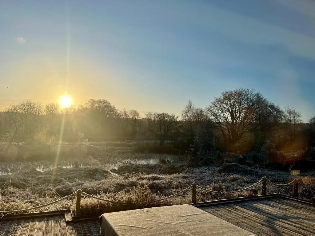 a sun rising over a field with a wooden bridge at Canal Side Cottage,on the banks of the Caledonian Canal in Inverness