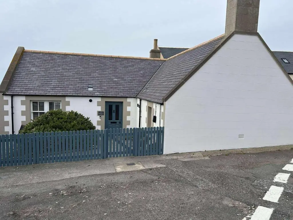 a white house with a blue fence in front of it at Findochty Beach house - Private Garden-BeachFront in Buckie