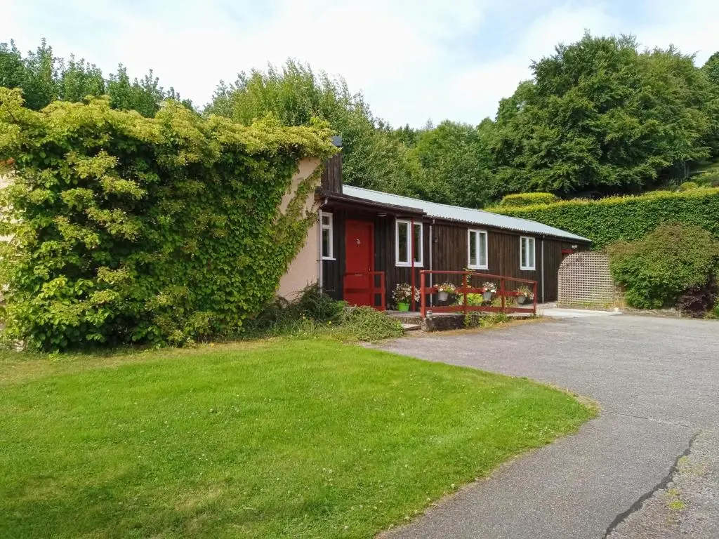 a house with a red door and a green yard at Strathpeffer Holiday Cottages in Strathpeffer