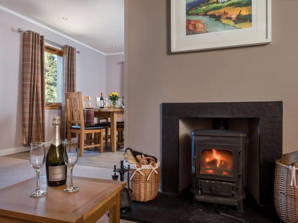 a living room with a fireplace and a table with wine glasses at Cairn Eilrig - Seasgair Lodges in Loch Morlich