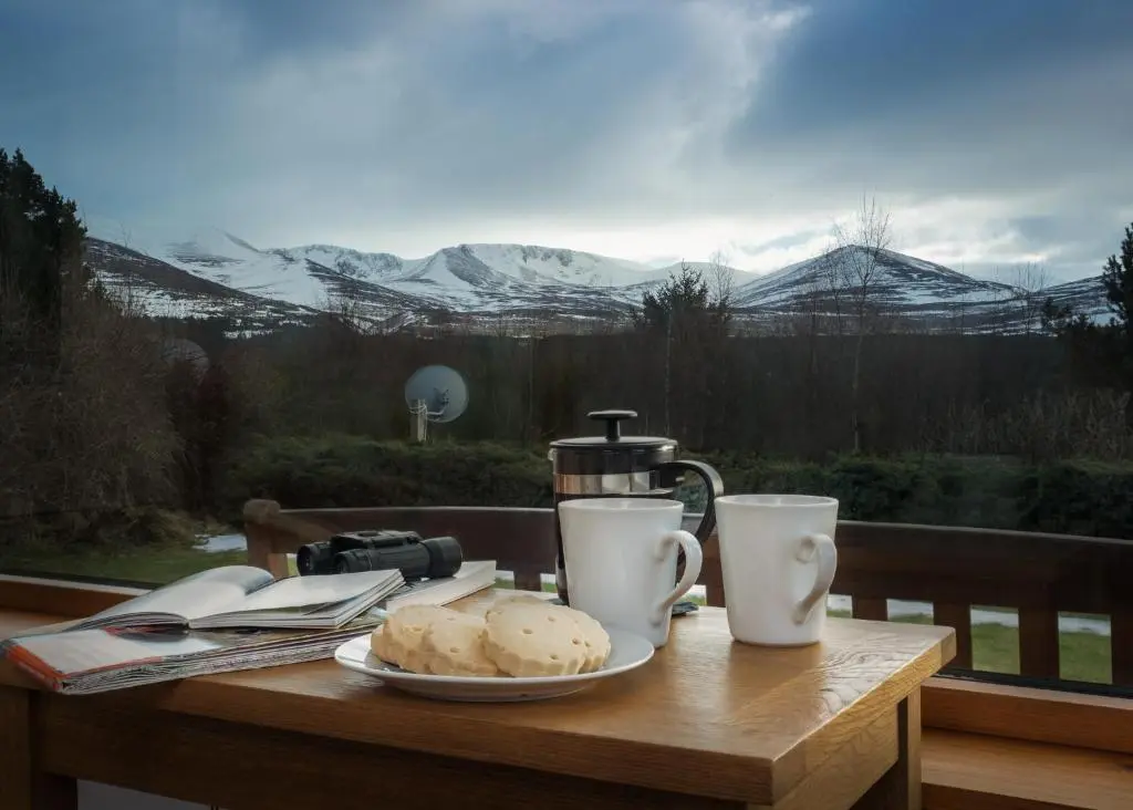 a table with a plate of food and two cups at Cairn Eilrig - Seasgair Lodges in Loch Morlich