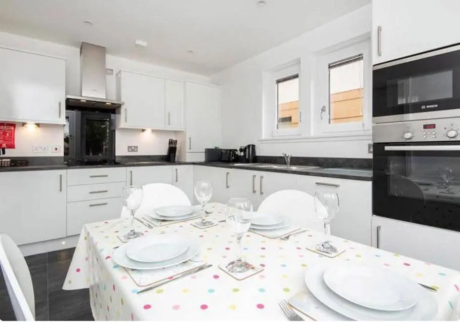 a white kitchen with a table with plates and wine glasses at 2 Bedroom Hedgefield Apartment 41-Free Parking in Inverness