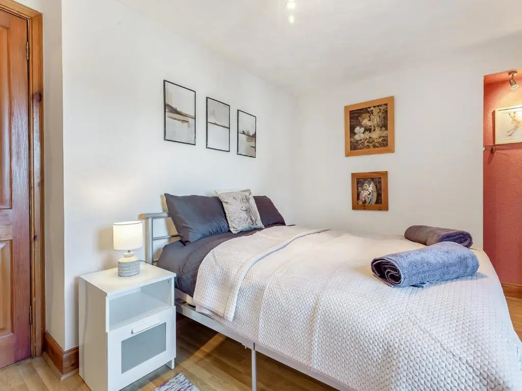 a white bedroom with a bed and a night stand at Ord Cottage in Kildary