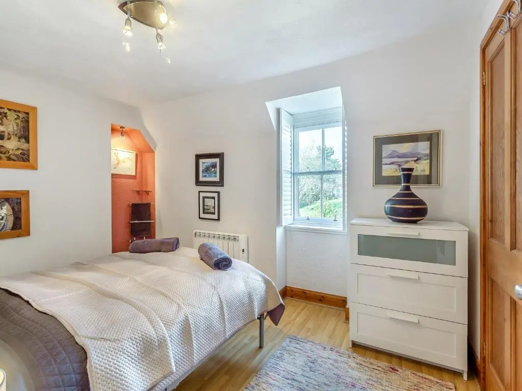 a bedroom with a bed with a dresser and a window at Ord Cottage in Kildary