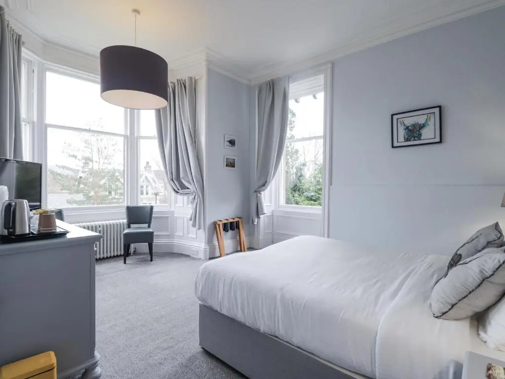 a white bedroom with a bed and a desk and window at Glenspey in Kingussie