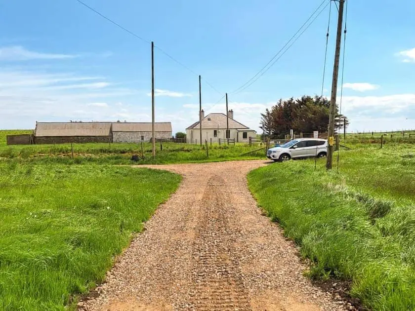 a dirt road with a car parked in a field at Auld House in Brora
