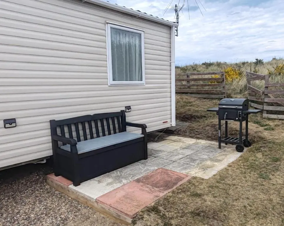 a bench sitting next to a house with a grill at Eagle's Den Caravan Holiday Retreat in Lossiemouth