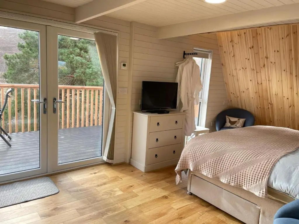 a bedroom with a bed and a television and a balcony at Little Getaway in the Highlands, private sauna and stargazing geodome in Garve