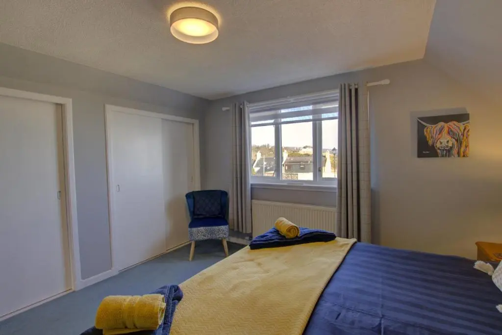a bedroom with a bed and a chair and a window at Beach Croft, Brora in Brora