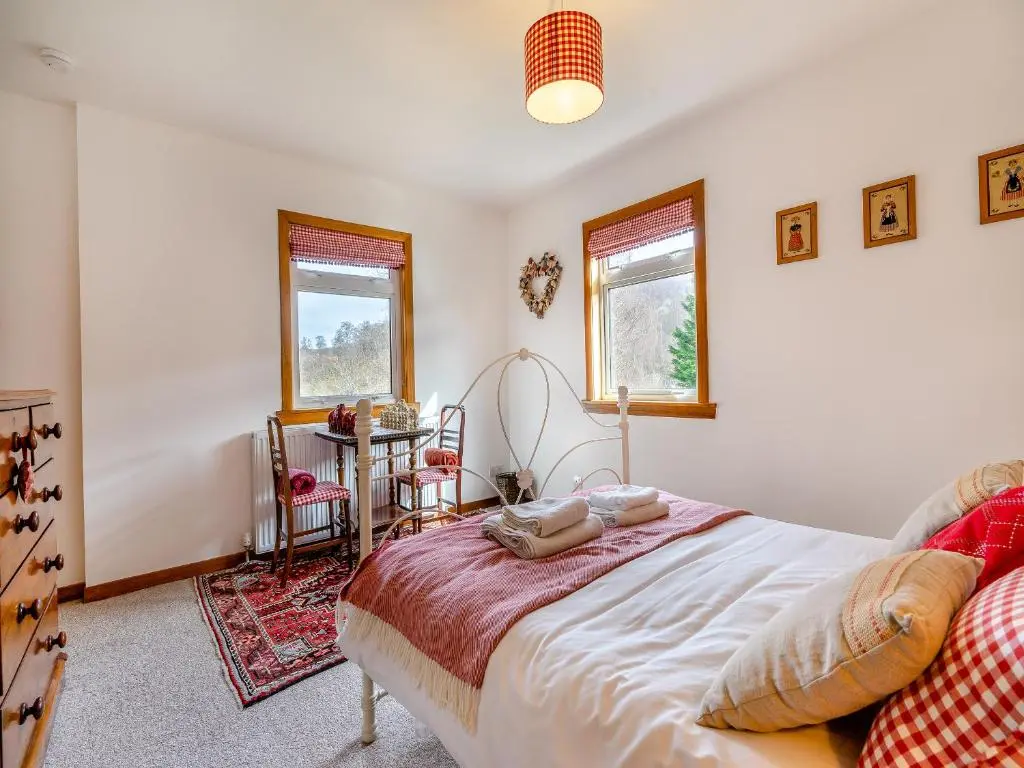 a bedroom with a bed and a table and two windows at Clunie Dam Lodge in Blair Atholl