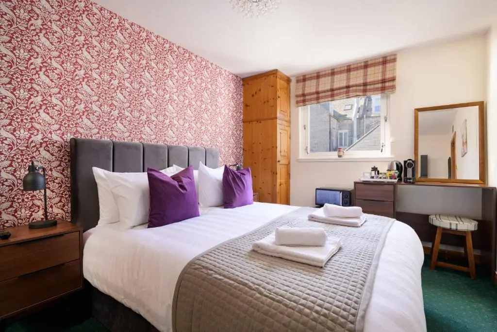 a bedroom with a large bed with purple pillows at Netherley Rooms in Ballater