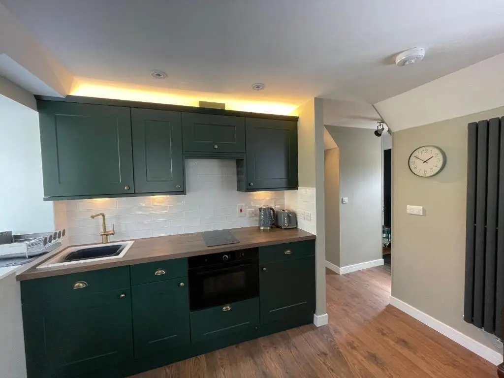 a kitchen with green cabinets and a clock on the wall at Struie Bothy near Dornoch Beach in Dornoch