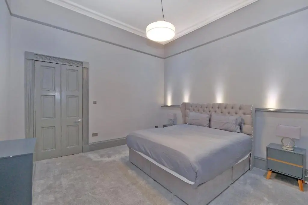 a white bedroom with a bed and a lamp at Kirkton House in Kirkton of Skene