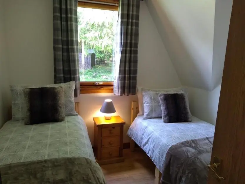 two beds in a small room with a window at True North Lodge - A cosy wee highland Getaway in Spean Bridge
