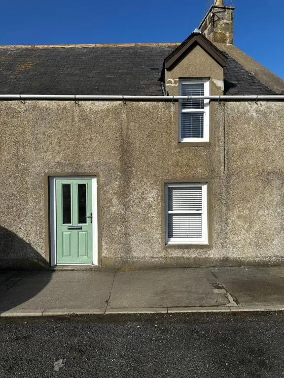 a building with a green door and two windows at Cozy Cottage Retreat in Portsoy