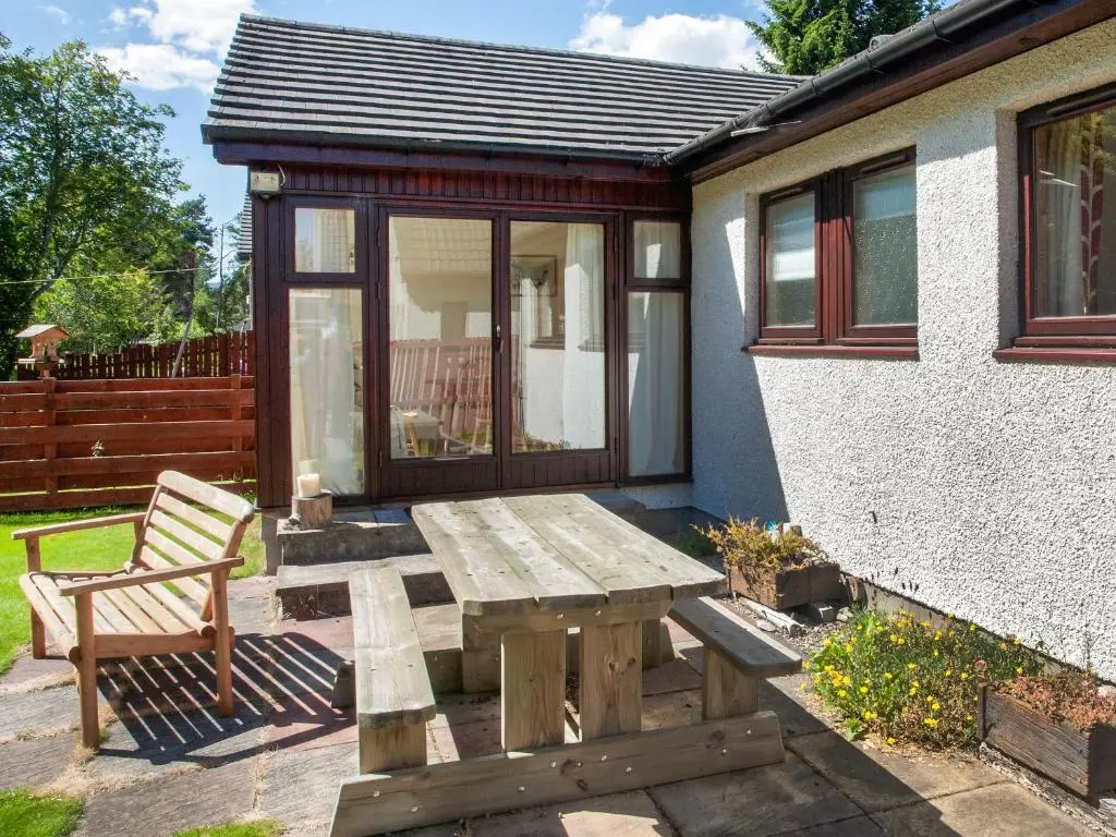 a wooden picnic table and a bench in front of a house at Heath Cottage in Boat of Garten