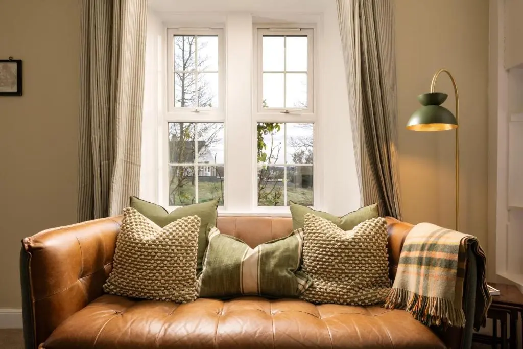 a brown leather couch with pillows in front of a window at Duffus House Lodge in Duffus