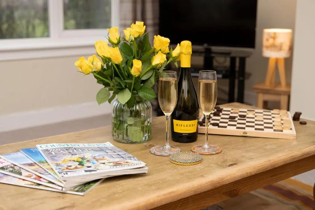 a table with a vase of yellow flowers and wine glasses at Kirktoun Cottage in Duffus