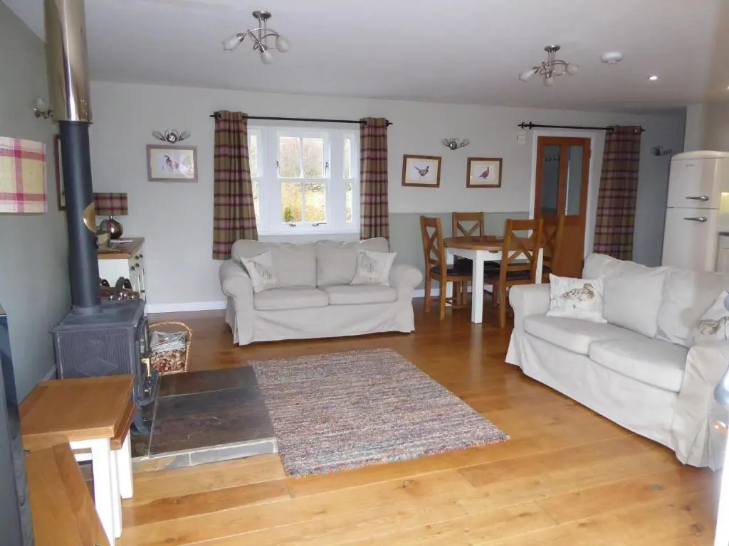 a living room with two white couches and a stove at Groose Hoose in Glenshee