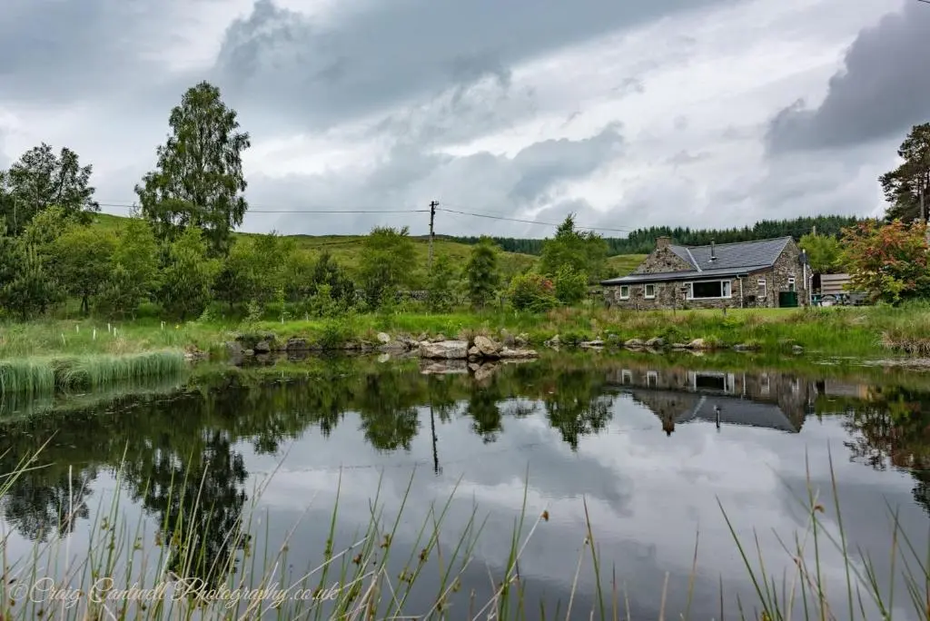 an old house and a pond in front of a house at Smiddy Cottage in Glenshee