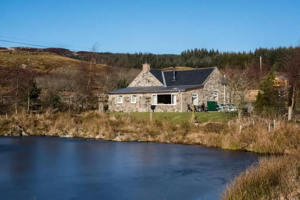 a stone house with a river in front of it at Smiddy Cottage in Glenshee