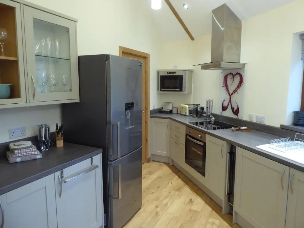 a kitchen with a stainless steel refrigerator and white cabinets at Scots Pine Treehouse in Glenshee