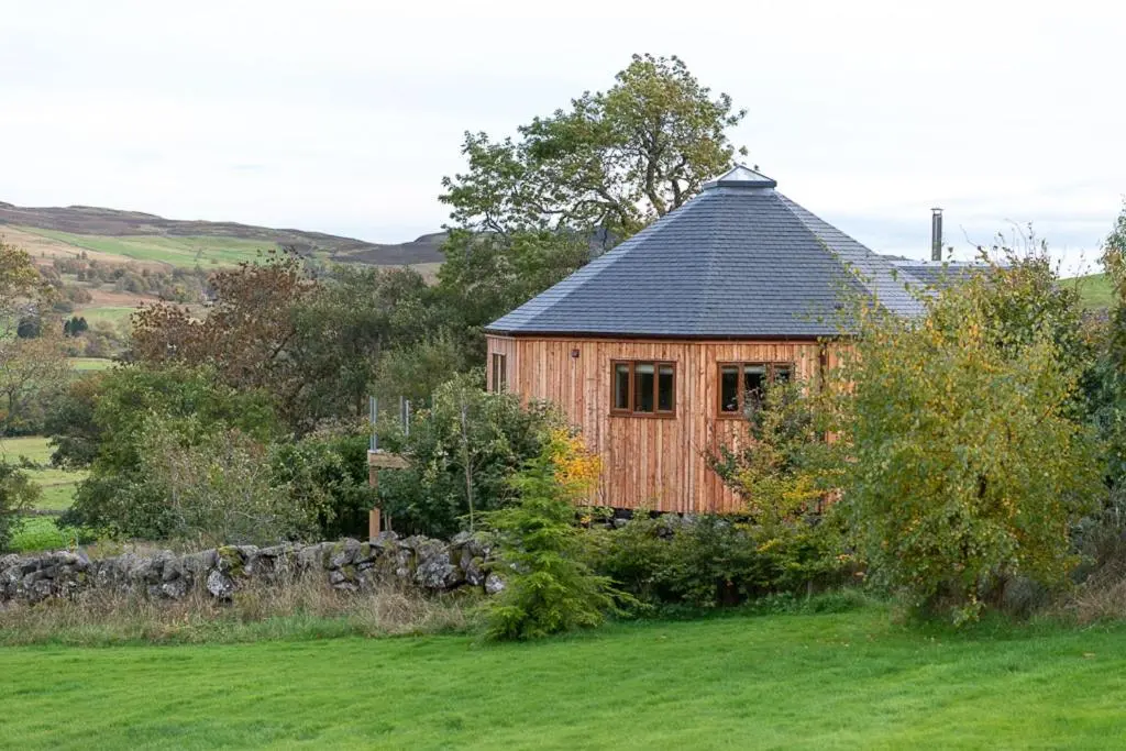 a wooden building with a black roof in a field at Silver Birch Treehouse in Glenshee